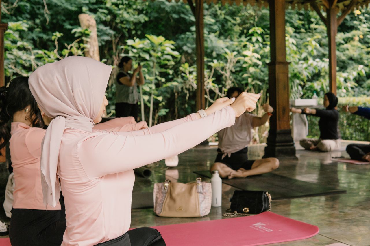 Menu Women practicing yoga outdoors in a serene pavilion setting in Indonesia.