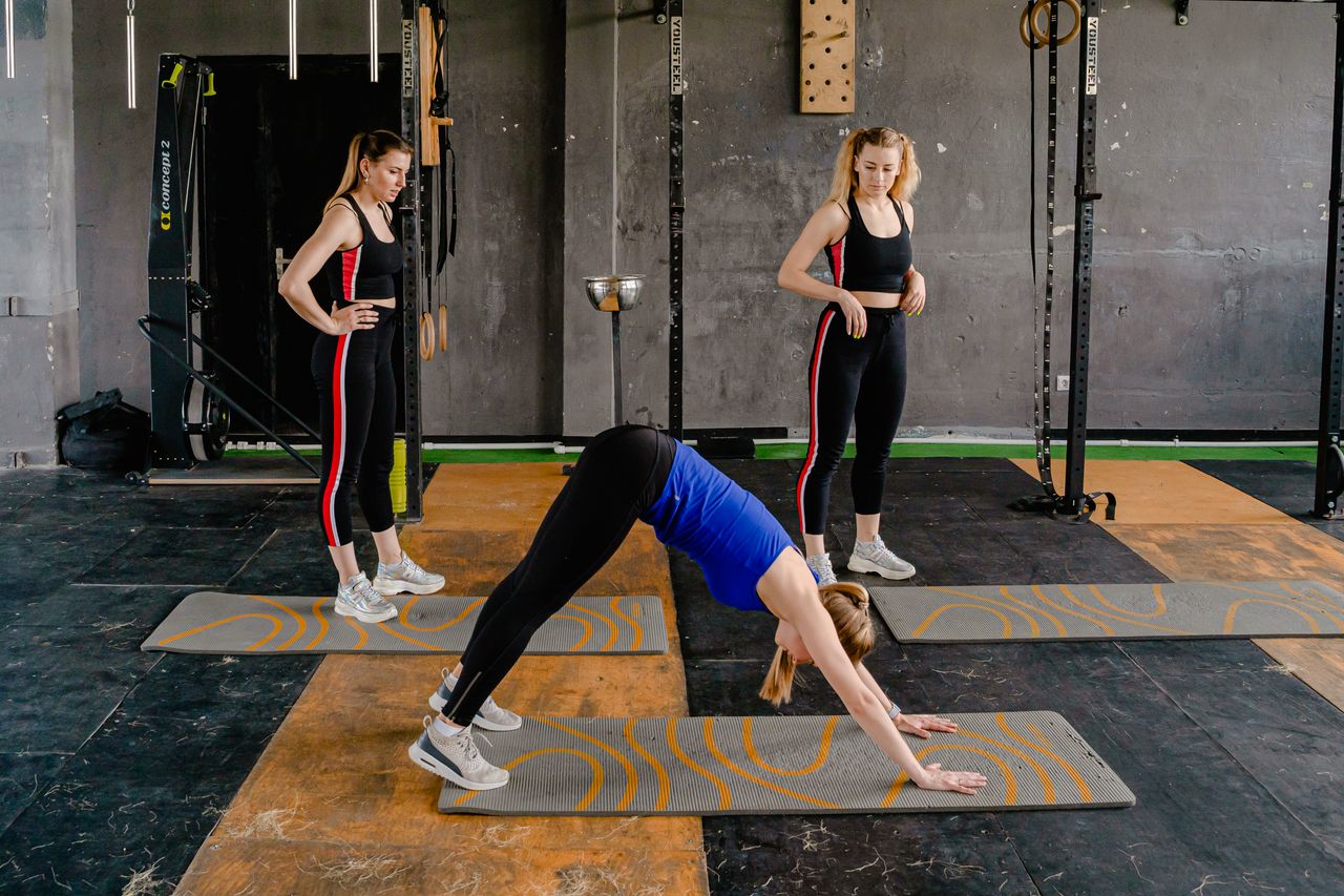 Home Three women engaged in yoga poses on mats in a gym environment, enhancing fitness and wellness.