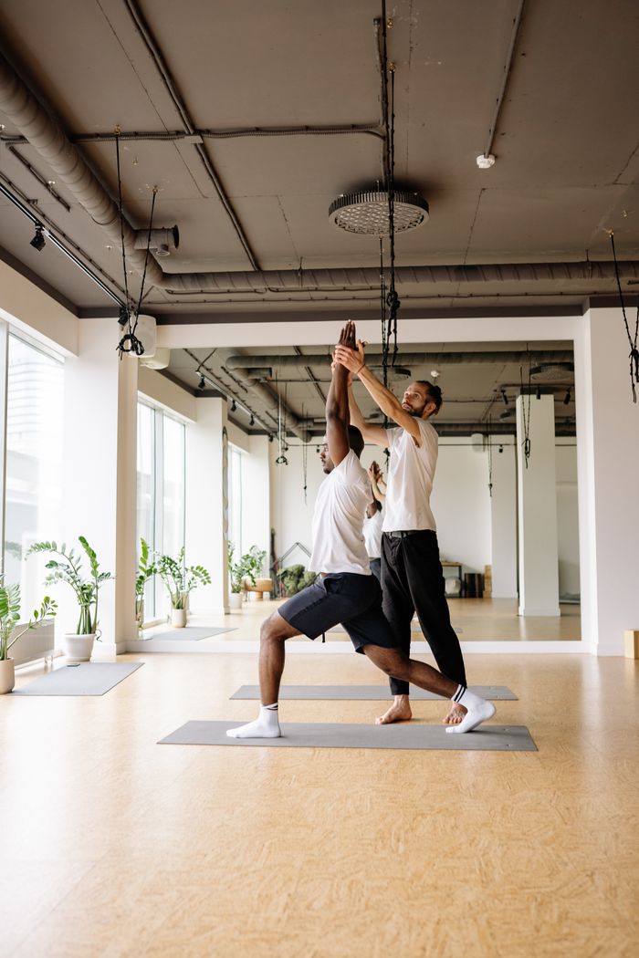 Home Yoga instructor helps a man stretch in a bright, modern studio.
